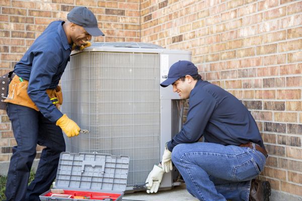 How Can I Be Sure I Hire the Best HVACR Company? Image shows two HVAC professionals working on a unit outside.