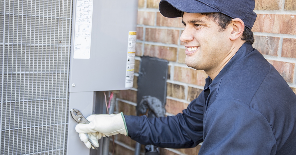 Blue collar air conditioner repairman at work.  The Latin descent man uses tools from his tool box as he begins work to repair or install an air conditioner unit at a customer's home.  He wears a blue uniform.