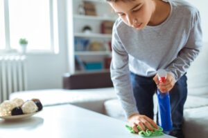 How to Reduce Dust in Your Home. A young child cleaning a counter with spray and a cloth.